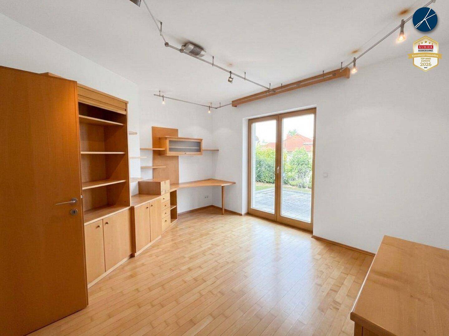 Helles Arbeitszimmer mit Holzboden, Einbauschränken und Zugang zum Außenbereich.