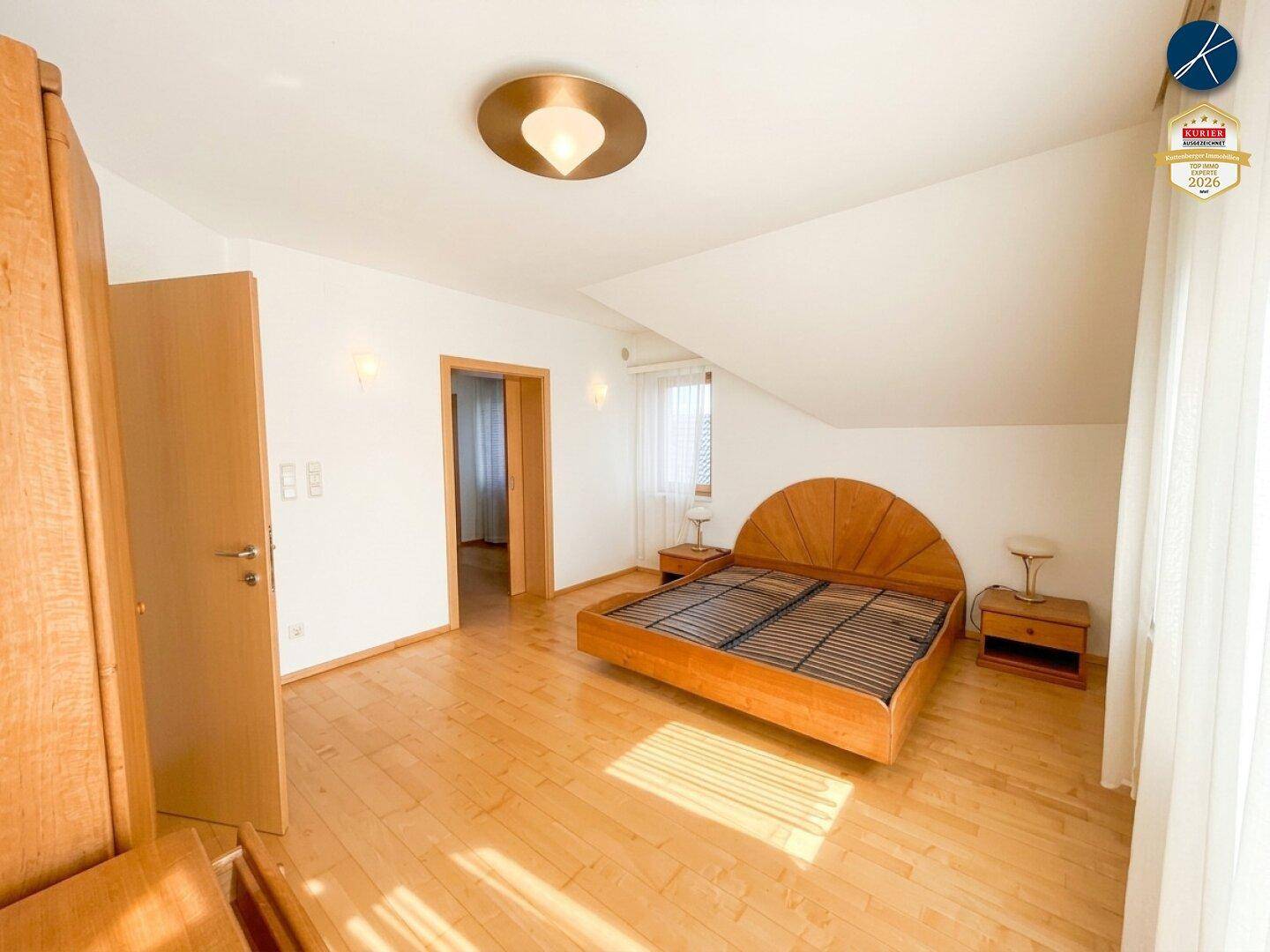 Geräumiges Schlafzimmer mit Holzboden, Doppelbett und Zugang zu einem weiteren Raum.