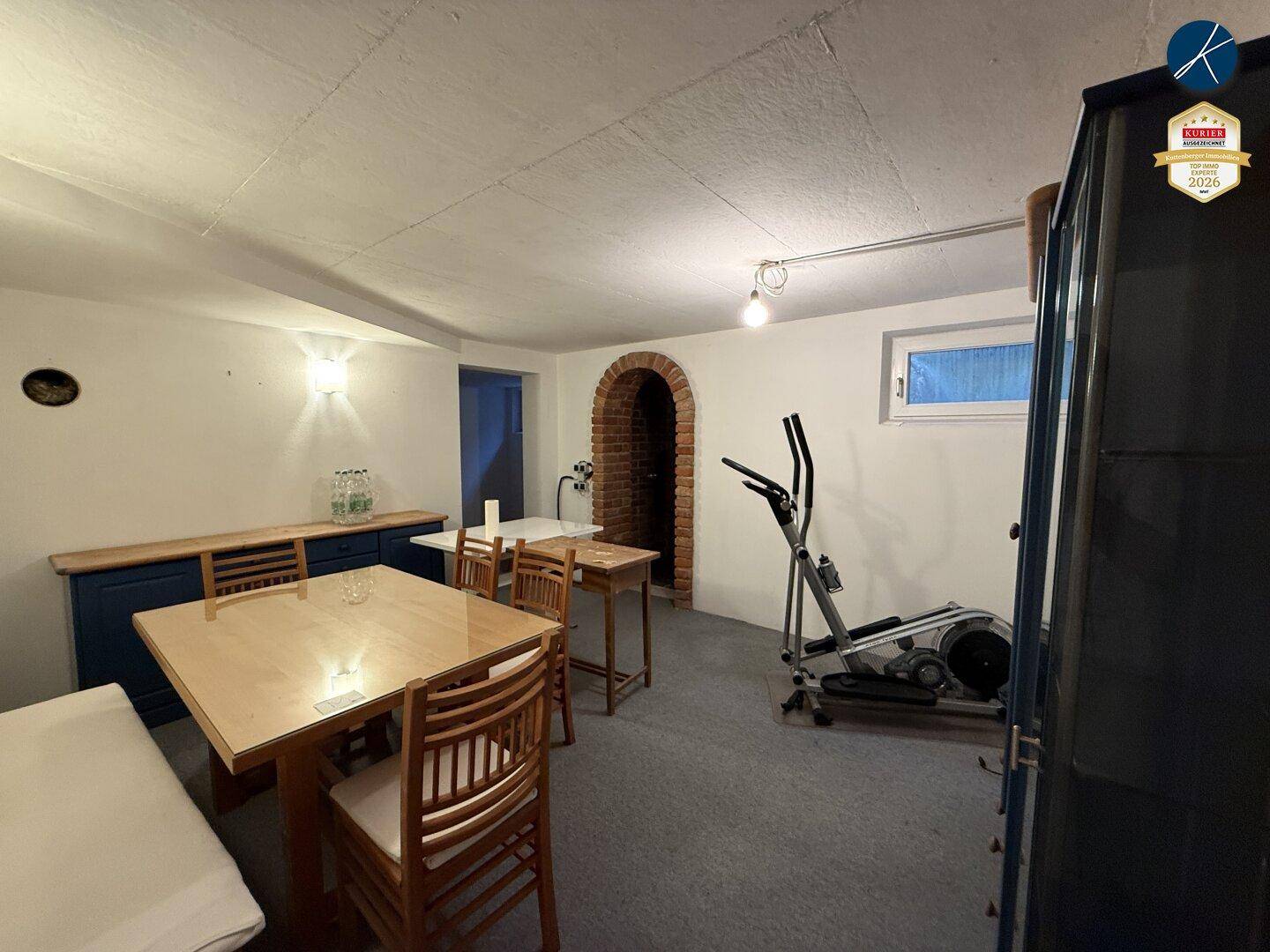 Vielseitiger Kellerraum mit Fitnessgeräten, Essbereich und rustikalem Ziegelbogen.