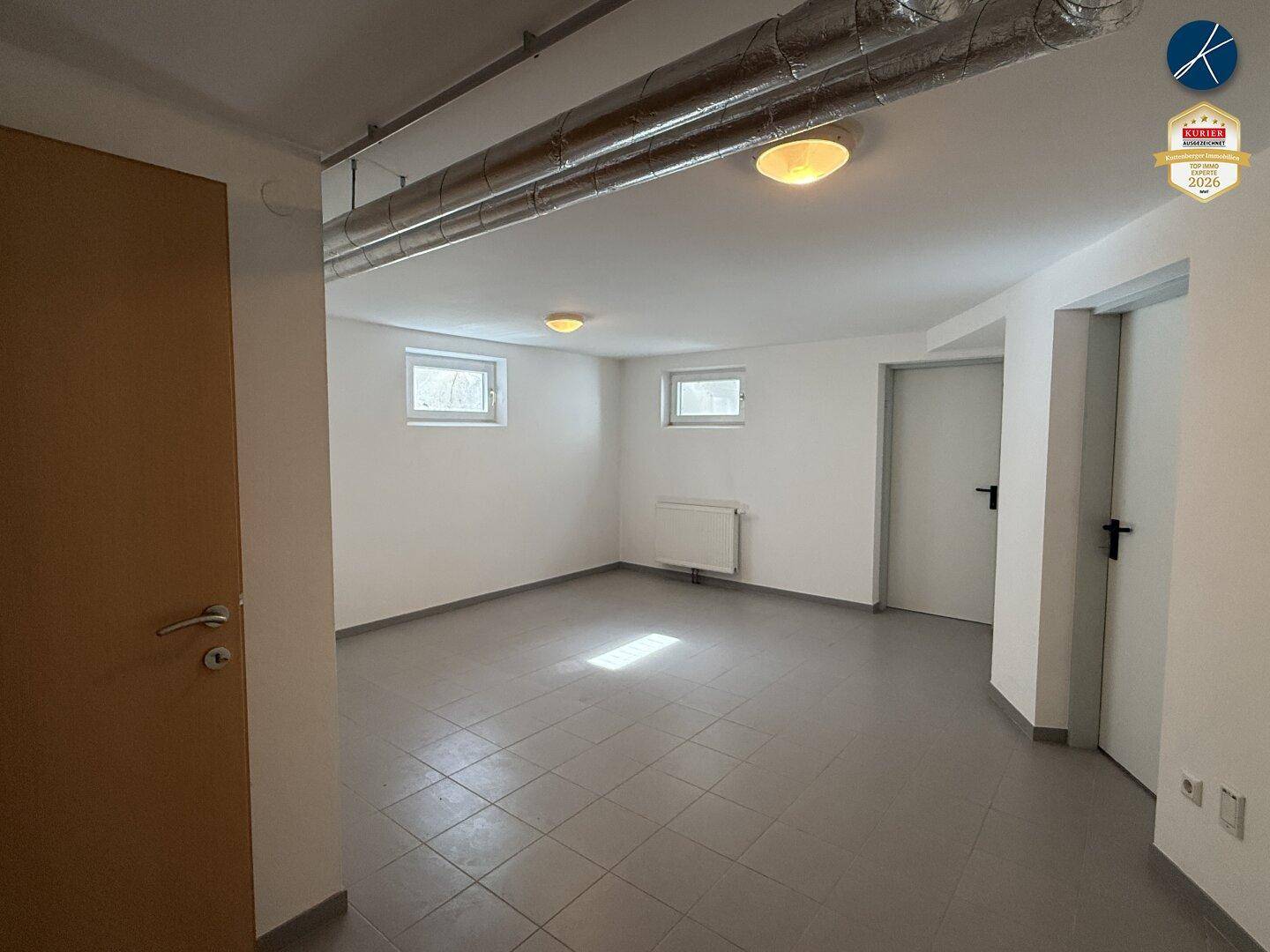 Heller Kellerraum mit Fliesenboden, Fenstern und Zugang zu weiteren Räumen.