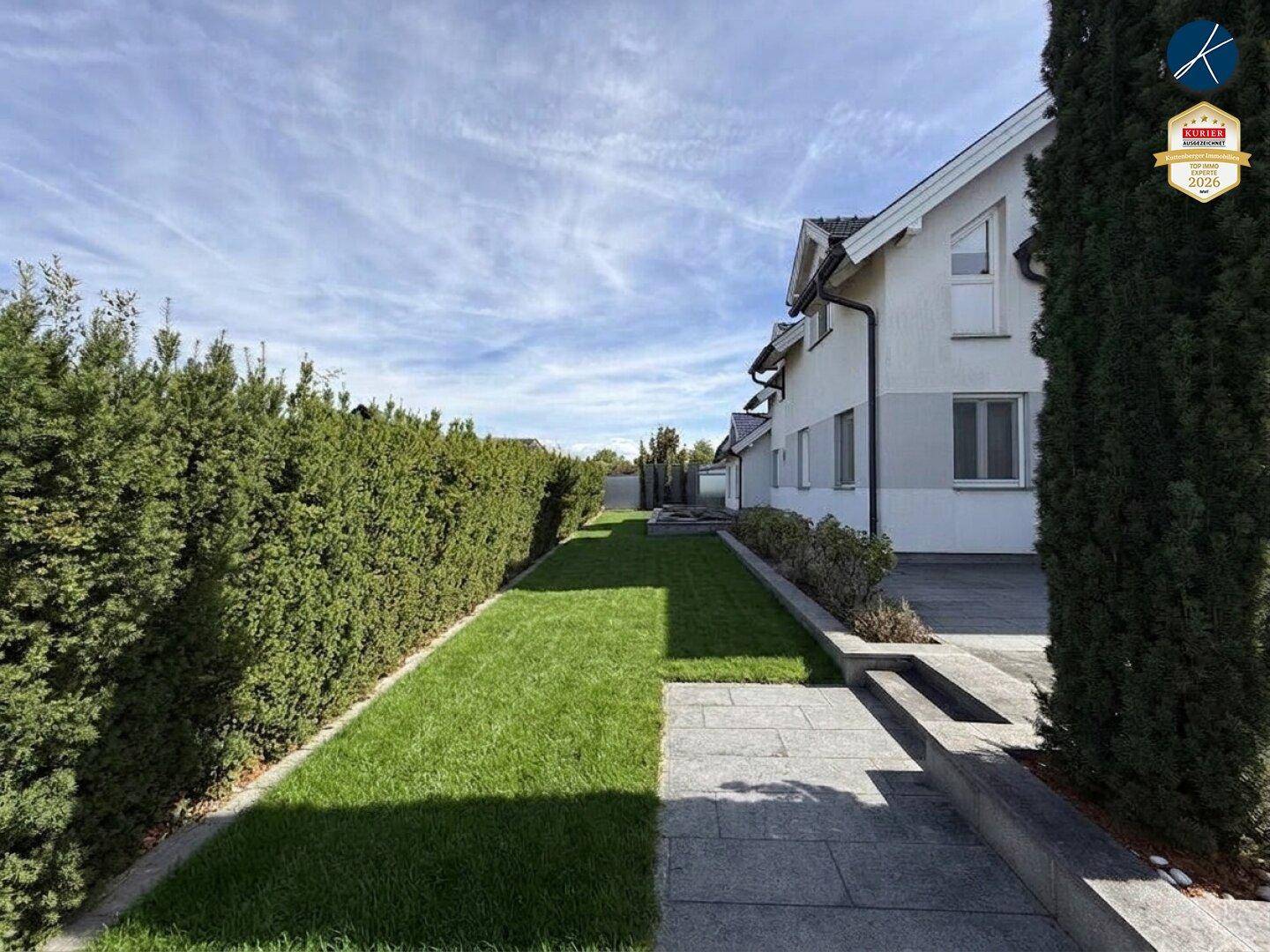 Gepflegter Gartenweg entlang des Hauses mit hoher Hecke und Rasenfläche.