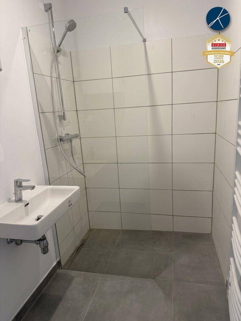 Modernes Badezimmer mit begehbarer Dusche, weißen Fliesen und einem Heizkörper.