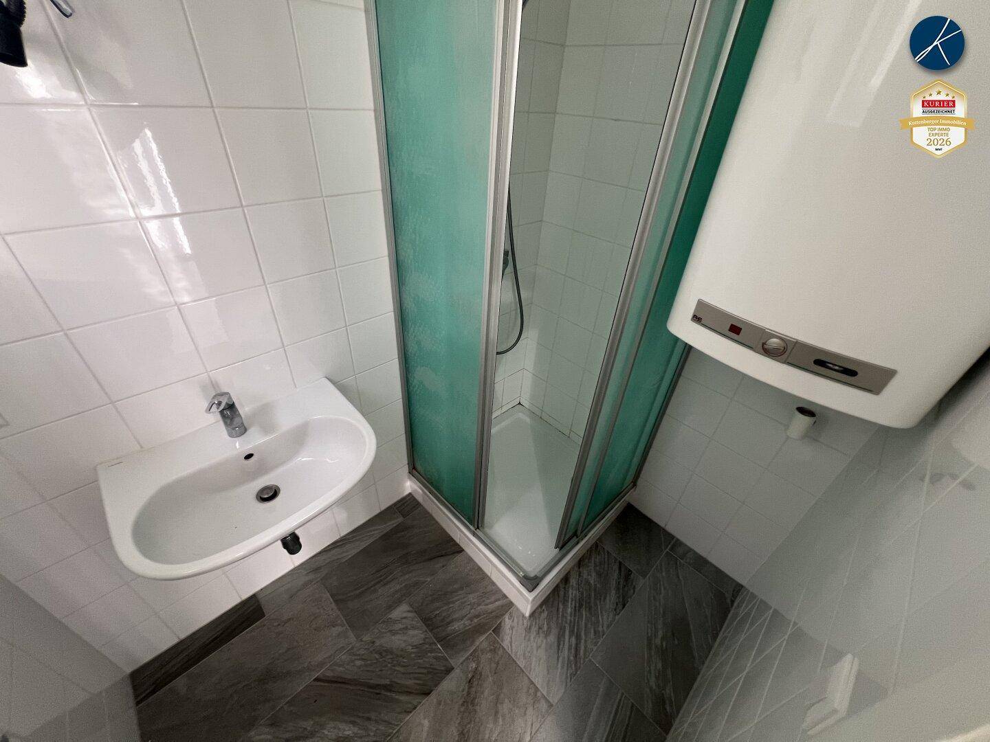 Kleines Badezimmer mit Duschkabine, Einzelwaschbecken, weißen Wandfliesen und Warmwasserboiler.
