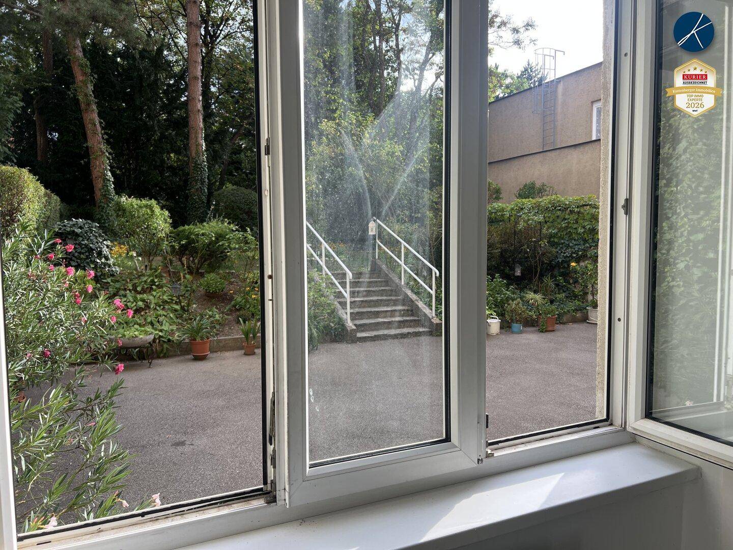 Blick aus dem Fenster auf den gepflegten Gartenbereich mit Treppe und üppiger Vegetation.