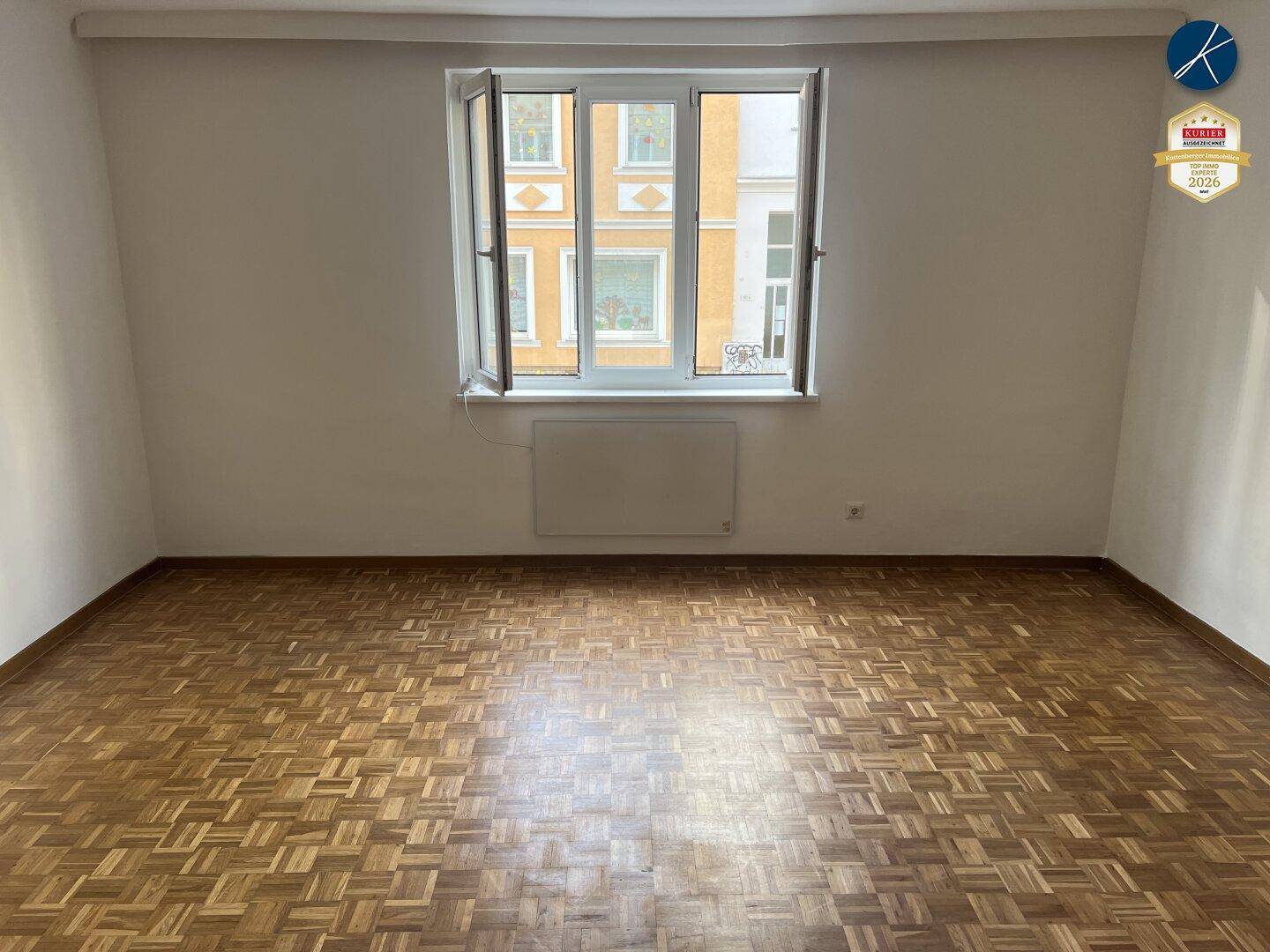 Leeres Zimmer mit klassischem Parkettboden und Fensterblick auf die gegenüberliegende Gebäudefassade.