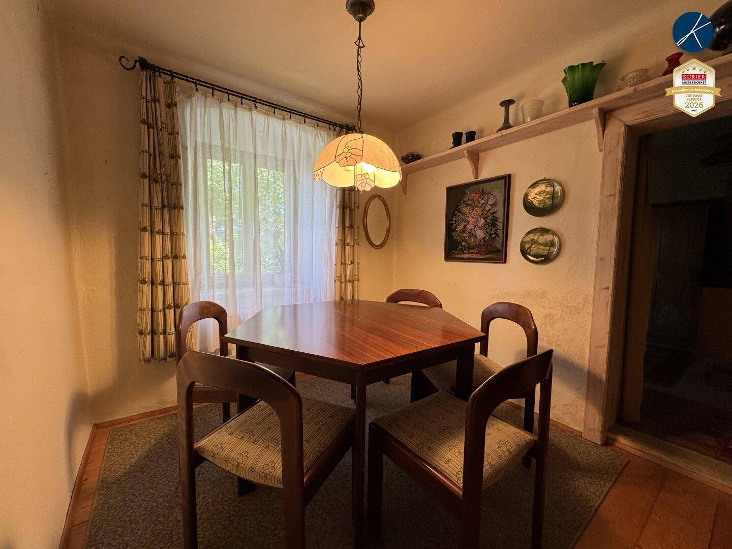 Gemütlicher Essbereich mit Holztisch, Stühlen und Fenster mit Vorhängen.