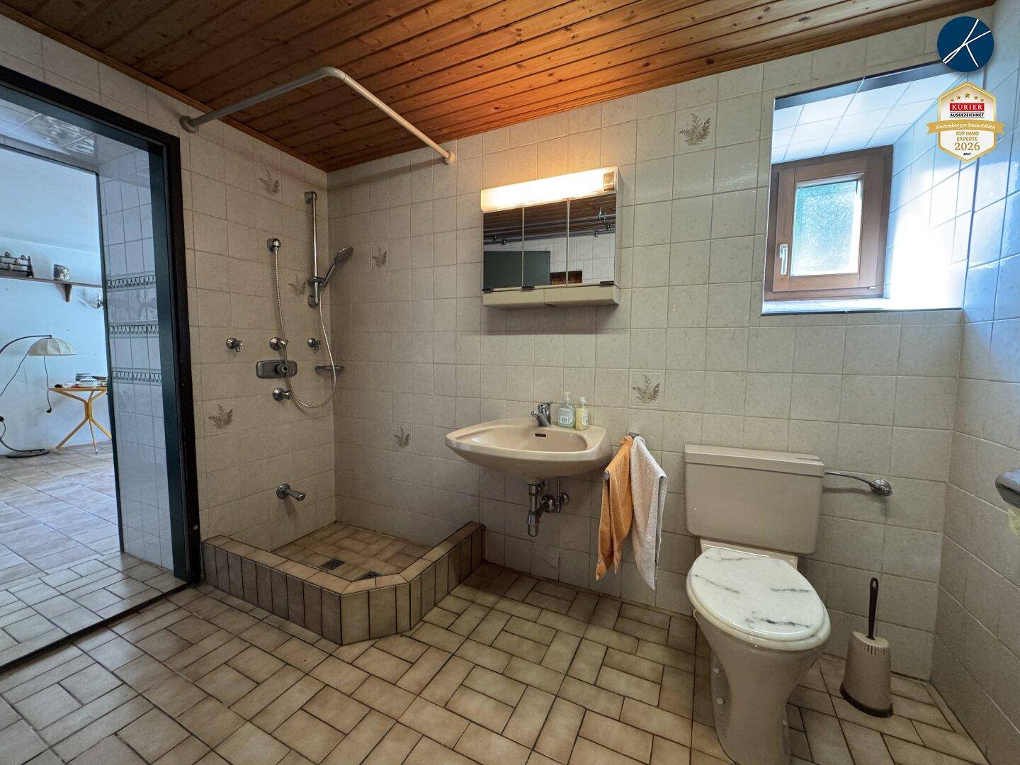 Badezimmer mit Dusche, Waschbecken, WC und gefliesten Wänden und Boden.