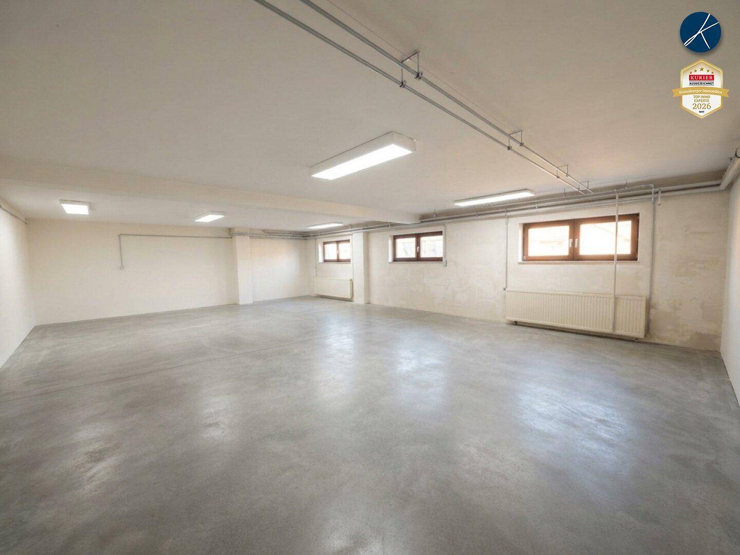 Großer, leerer Raum im Untergeschoss mit Betonboden, Heizkörpern und sichtbaren Deckeninstallationen.