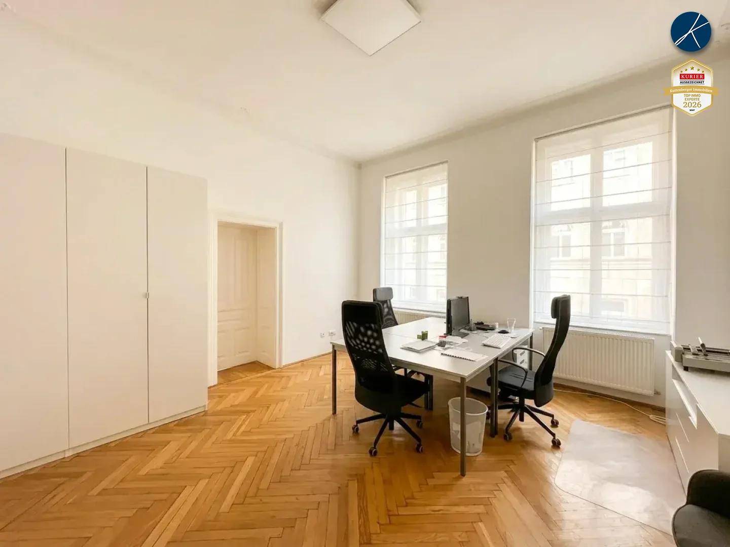 Heller Büroraum mit funktionalen Arbeitsplätzen, weißen Schränken und klassischem Fischgrätparkettboden.
