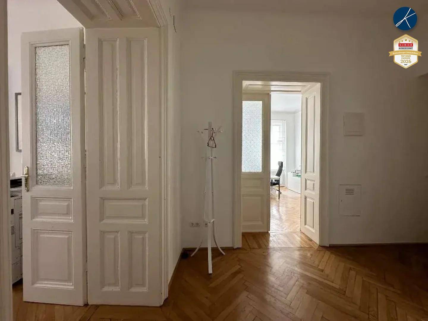 Heller Flur mit mehreren klassischen Türen, teilweise mit Glaseinsätzen, und Fischgrätparkettboden.