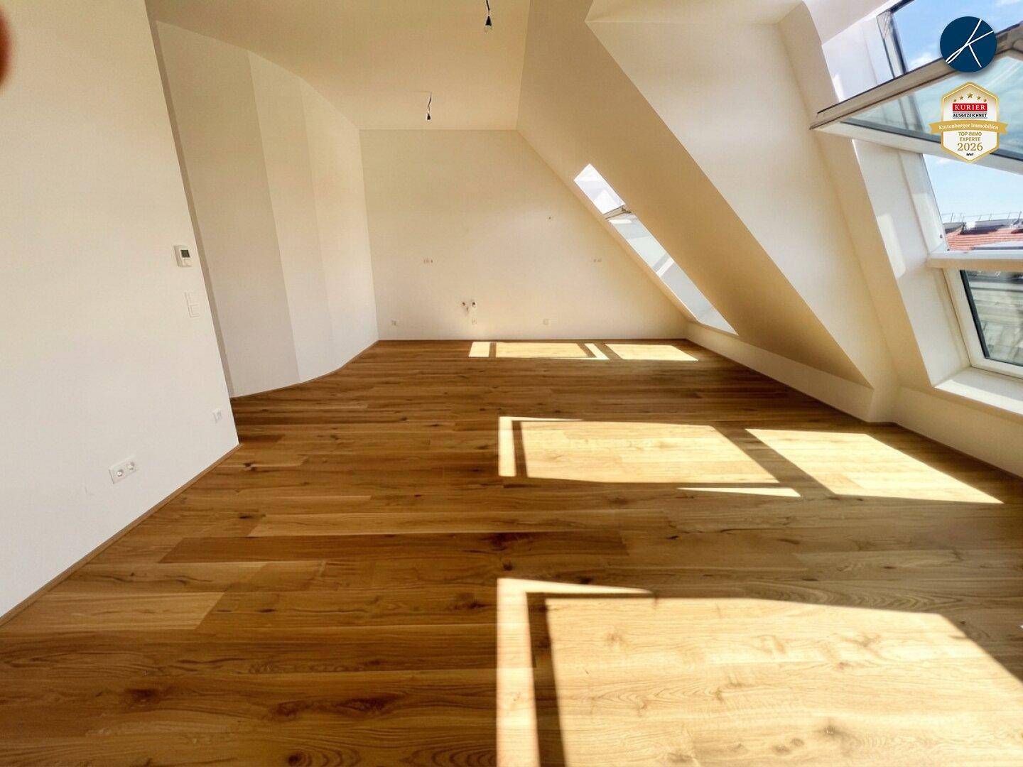 Geräumiges Dachgeschosszimmer mit Holzboden und schrägen Wänden, durchflutet von natürlichem Licht.