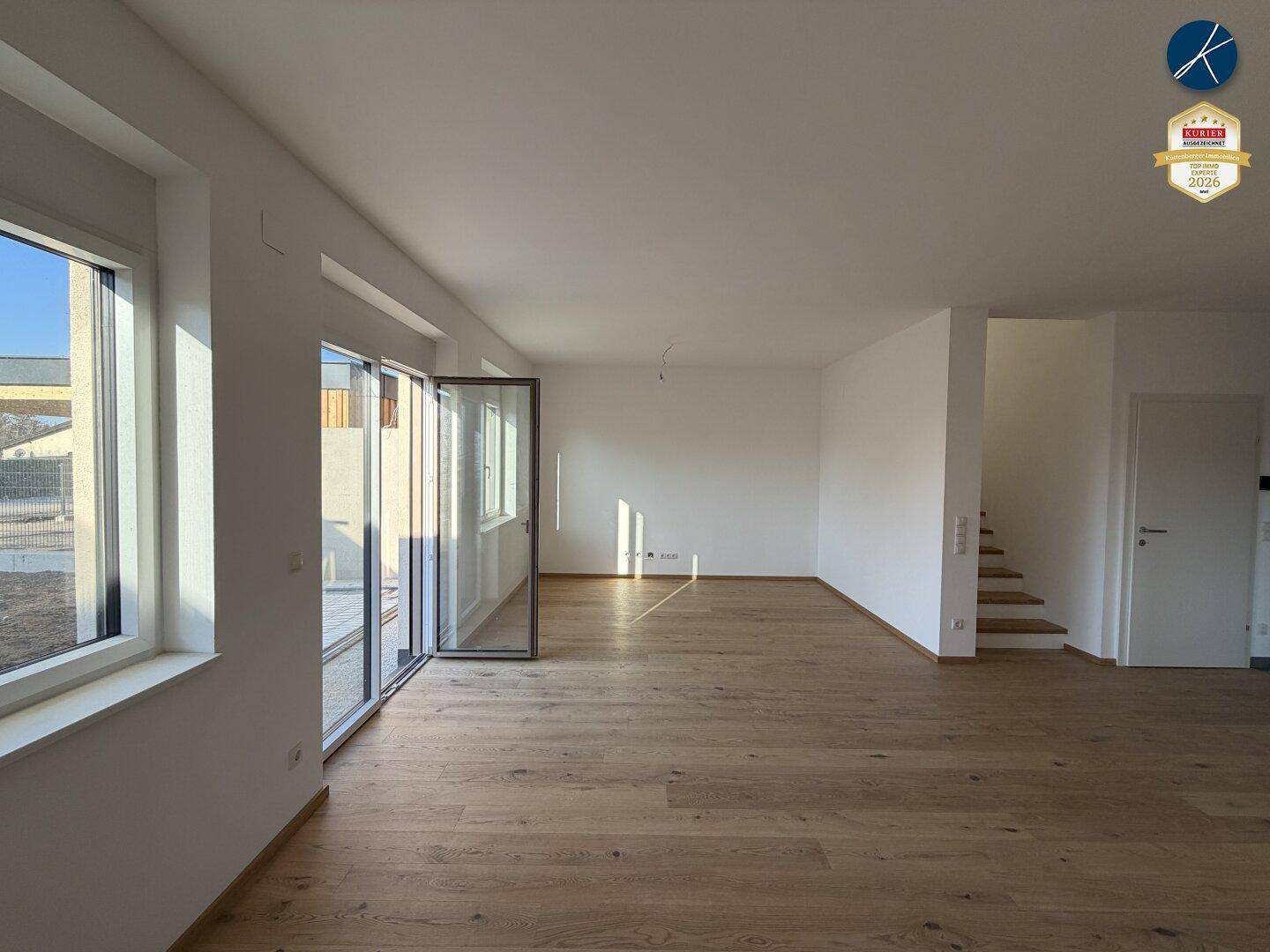 Heller, unmöblierter Wohnbereich mit großen Fenstern, Zugang zur Terrasse und Eichenparkettboden.