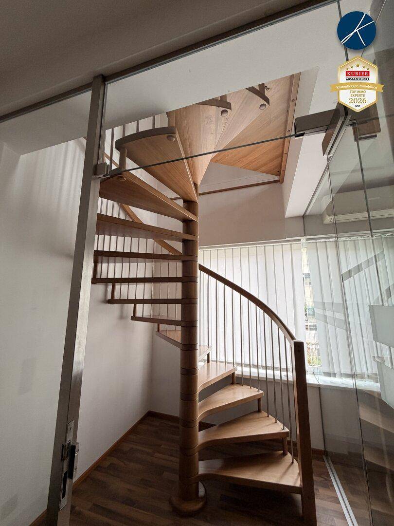 Elegante Holzwendeltreppe mit Metallgeländer, sichtbar durch eine Glasabtrennung, auf Laminatboden.
