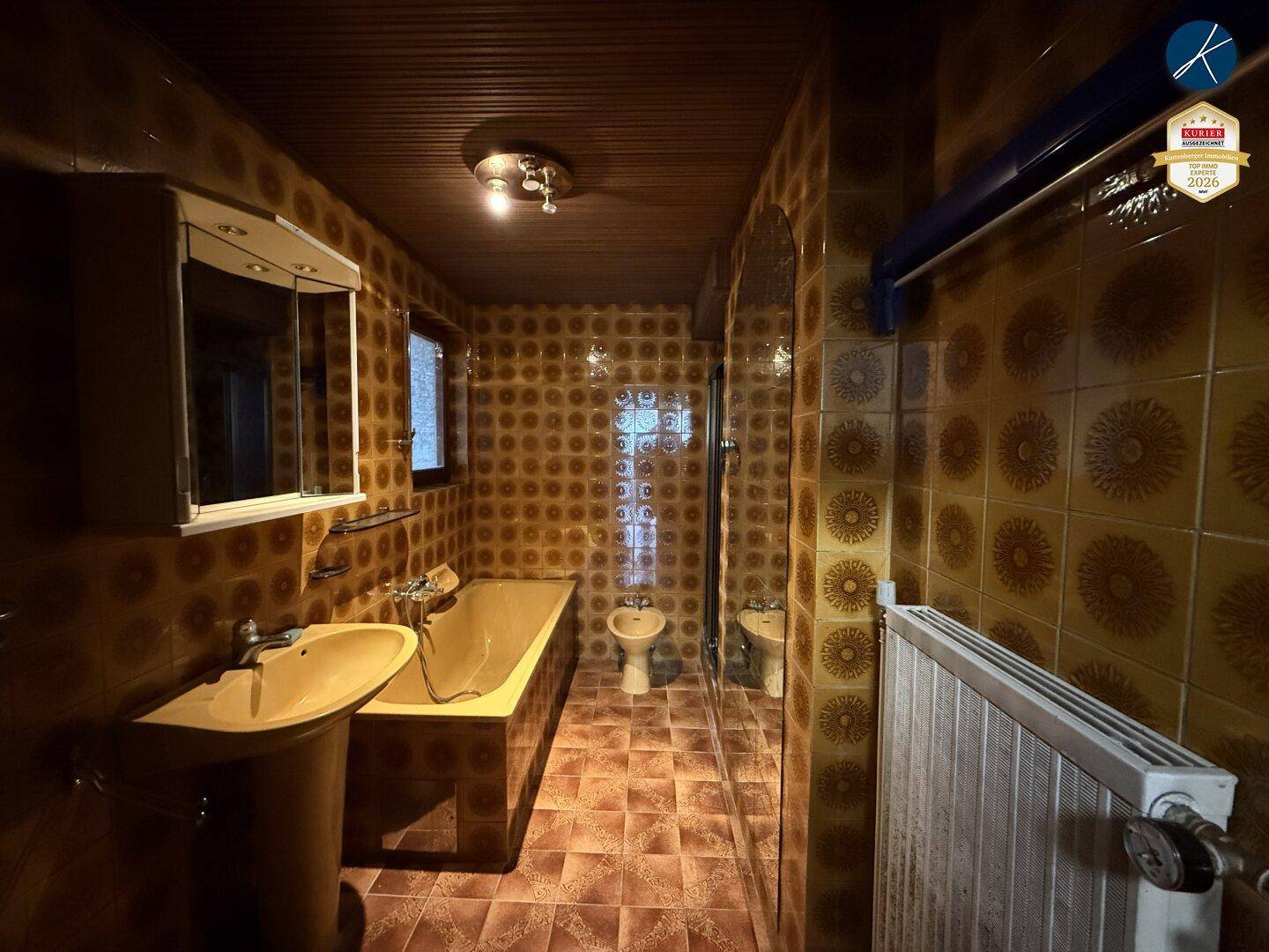 Badezimmer mit braunen gemusterten Fliesen, Badewanne, Bidet und WC, im Stil der 80er Jahre.