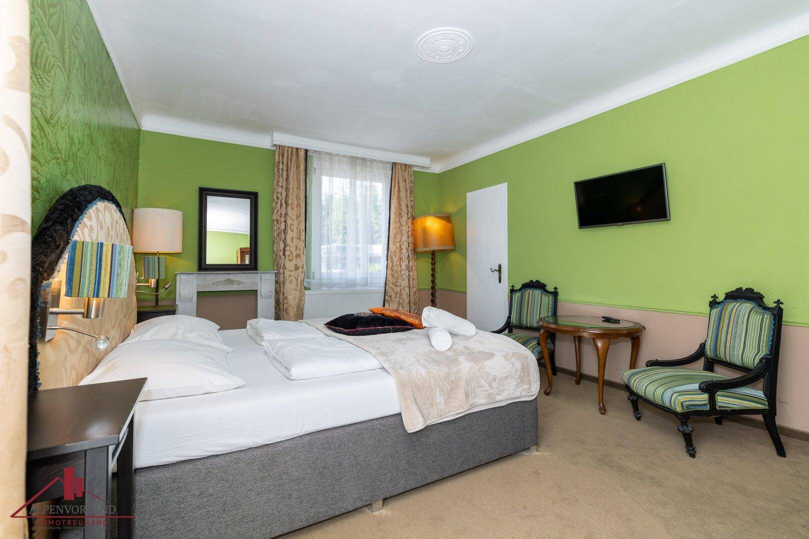 Helles Schlafzimmer mit grün gestrichenen Wänden, Doppelbett und traditionellen Möbeln.