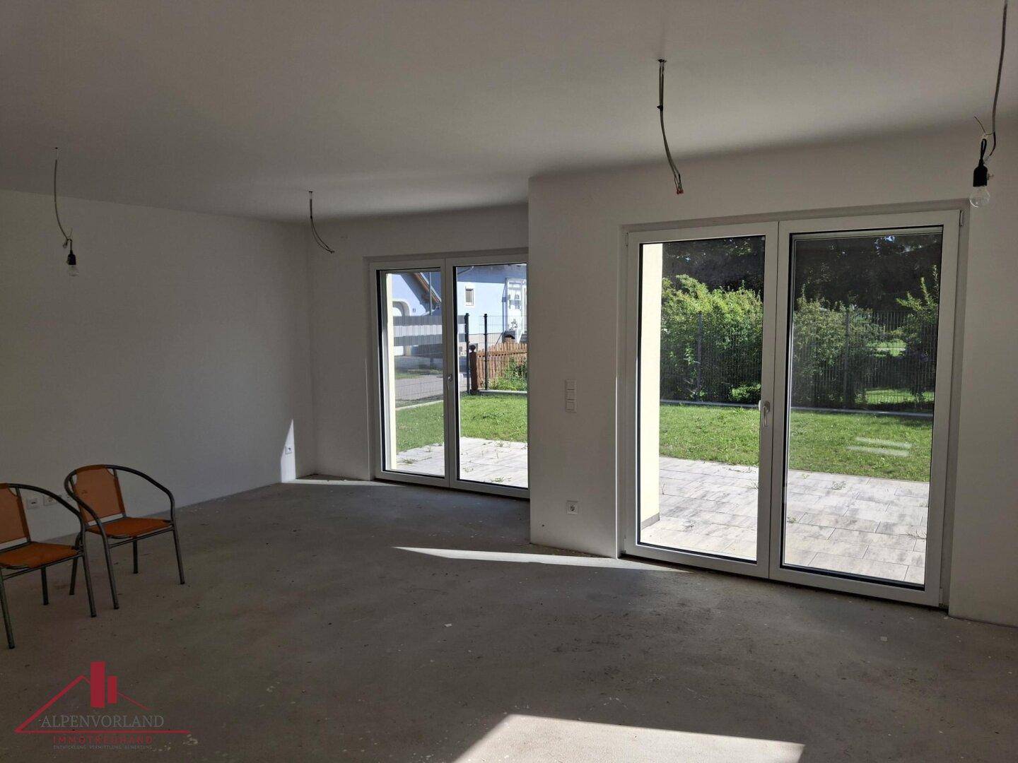 Unfertiger Wohnbereich mit großen Fenstertüren, die Zugang zur Terrasse und zum Garten bieten.