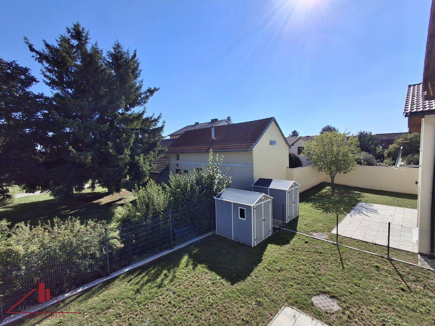 Weitläufiger Garten mit zwei Gartenhäusern, hohen Bäumen und viel Sonnenlicht.