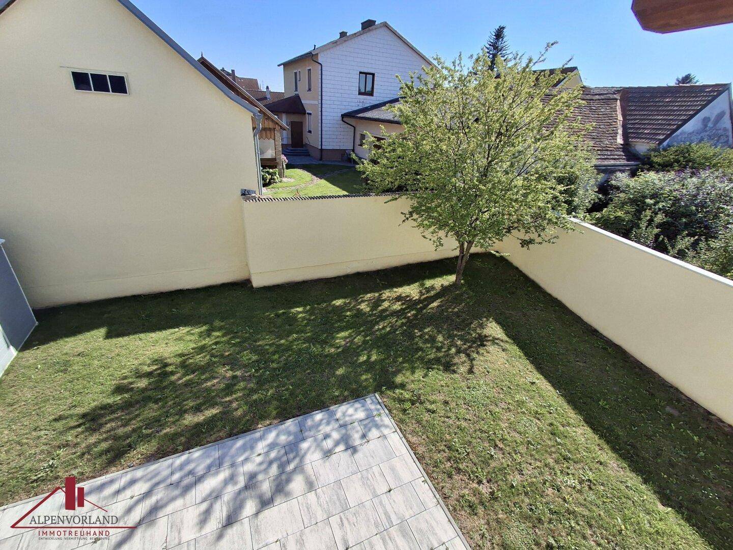 Gepflegter Gartenbereich mit Rasenfläche, einem Baum und einer gepflasterten Terrasse.