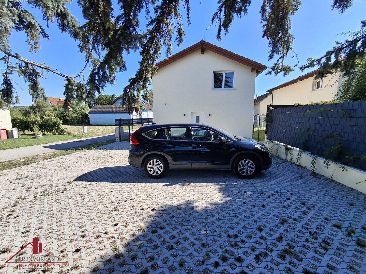Außenansicht des Hauses mit einem gepflasterten Parkplatz und einem geparkten Auto.