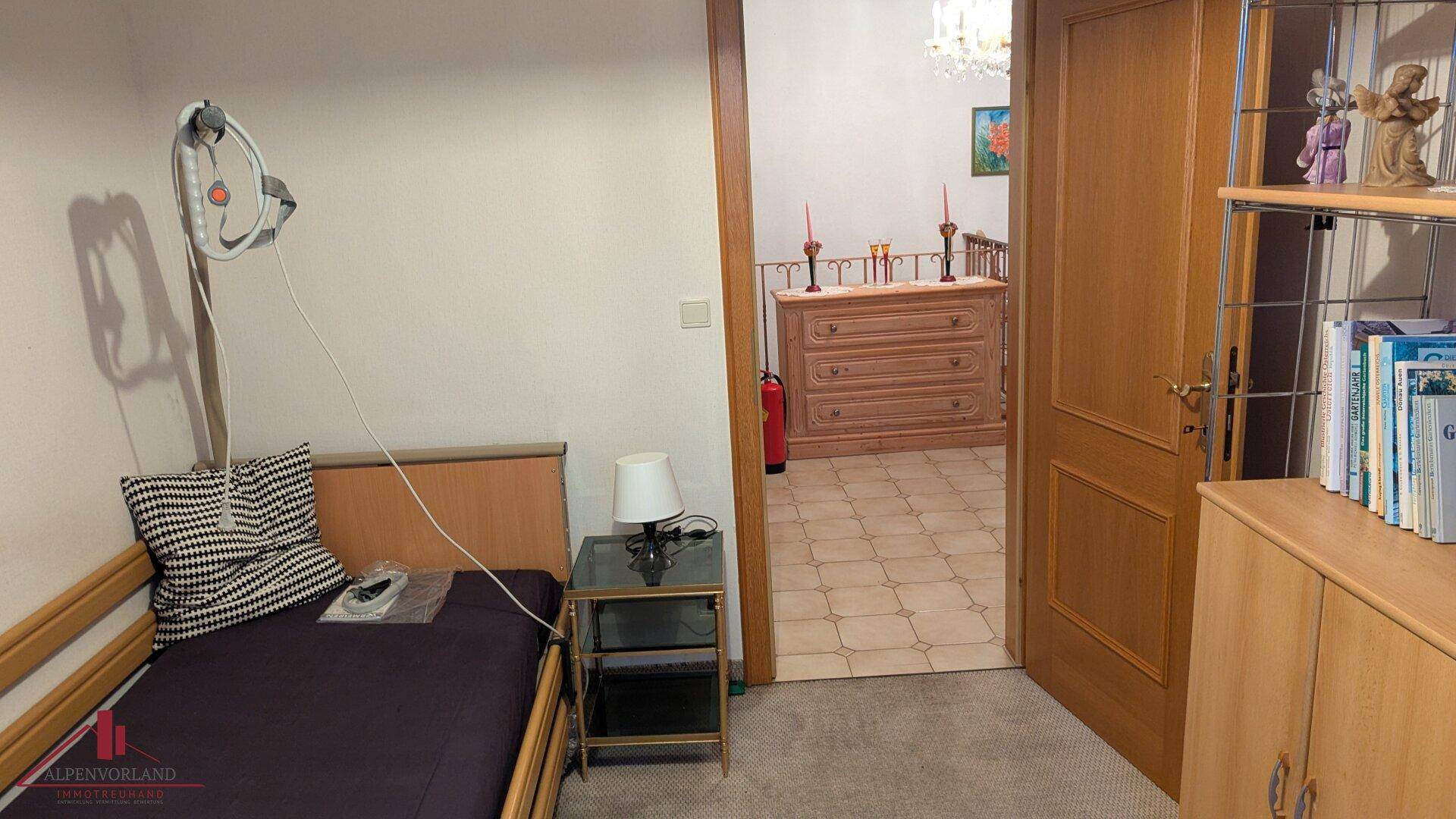 Einfaches Schlafzimmer mit Einzelbett und Teppichboden, mit Blick in den Flur.