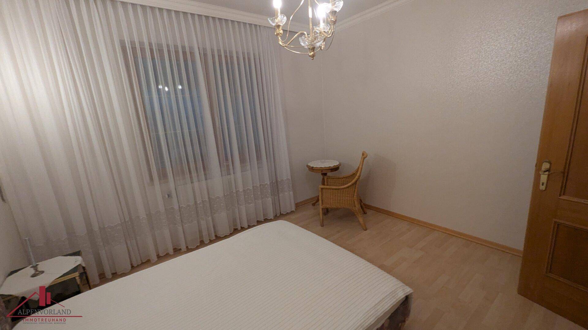 Schlafzimmer mit Laminatboden, großem Fenster und klassischem Kronleuchter.