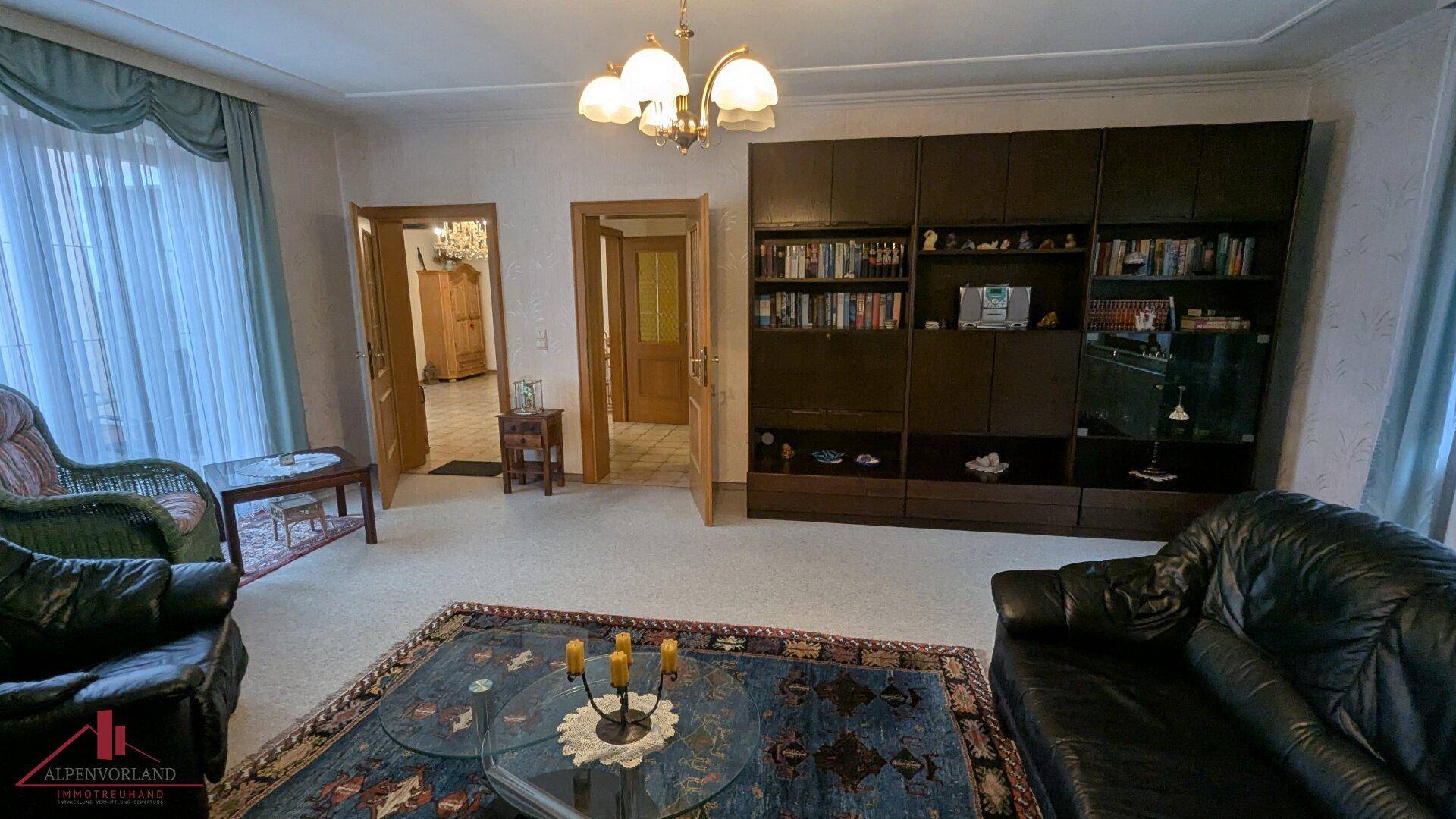 Geräumiges Wohnzimmer mit Teppichboden, Ledersofas und Blick auf den Außenbereich durch große Fenster.