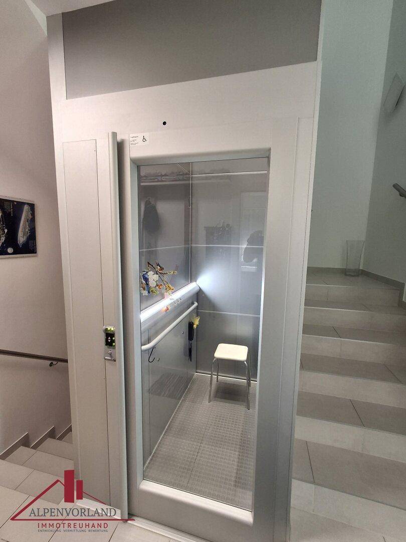 Moderner Aufzug im Treppenhaus mit Glasfront und Haltegriffen für Barrierefreiheit.