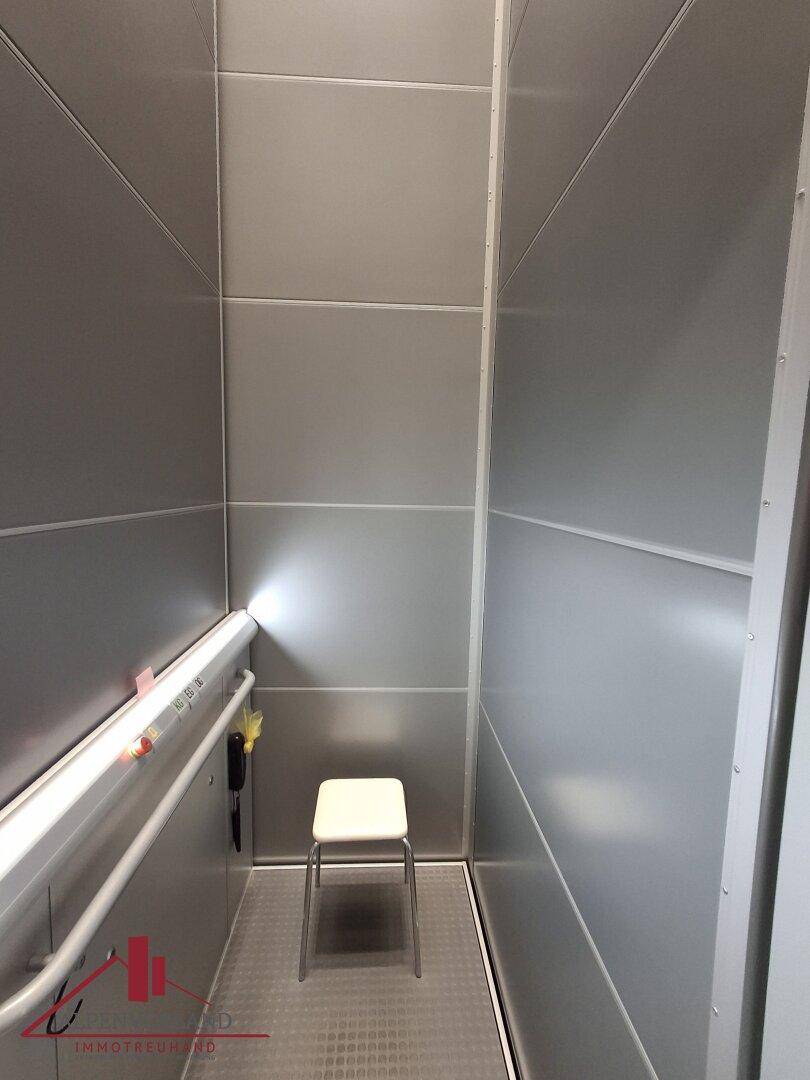 Innenansicht der Aufzugskabine mit einem kleinen Sitz und Haltegriff.
