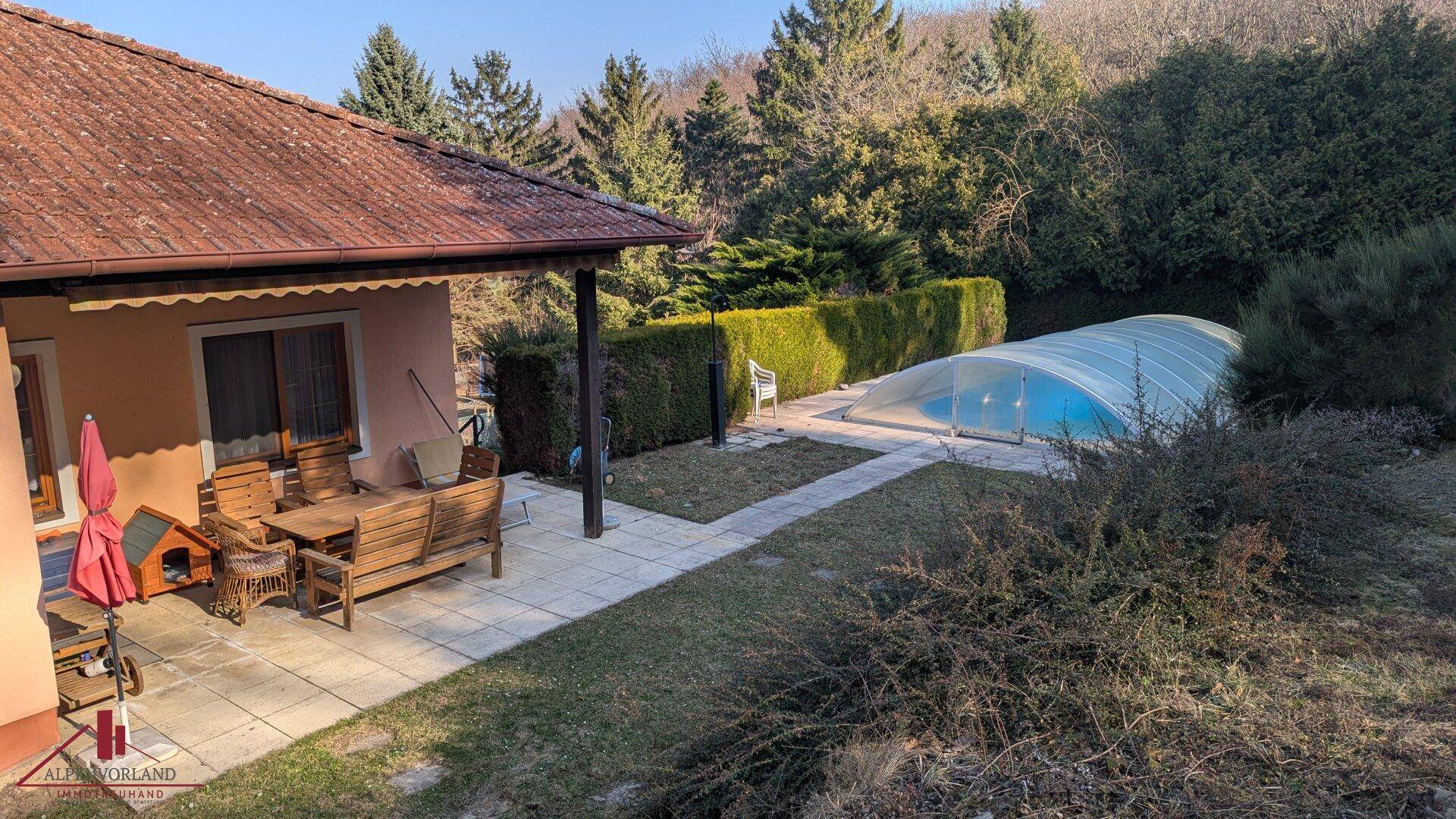 Hinterhof mit überdachtem Pool, angrenzender Terrasse und üppiger grüner Landschaft.