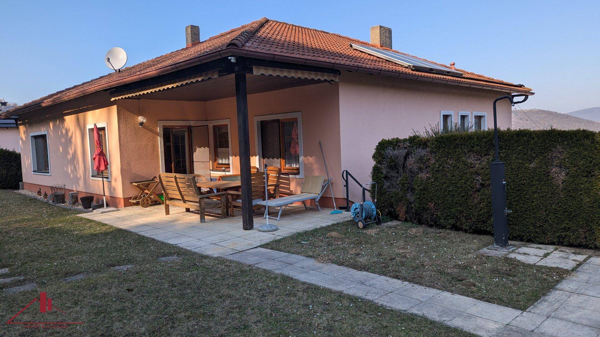 Gemütliche Terrasse am Haus mit Gartenmöbeln, umgeben von Rasen und Hecken.