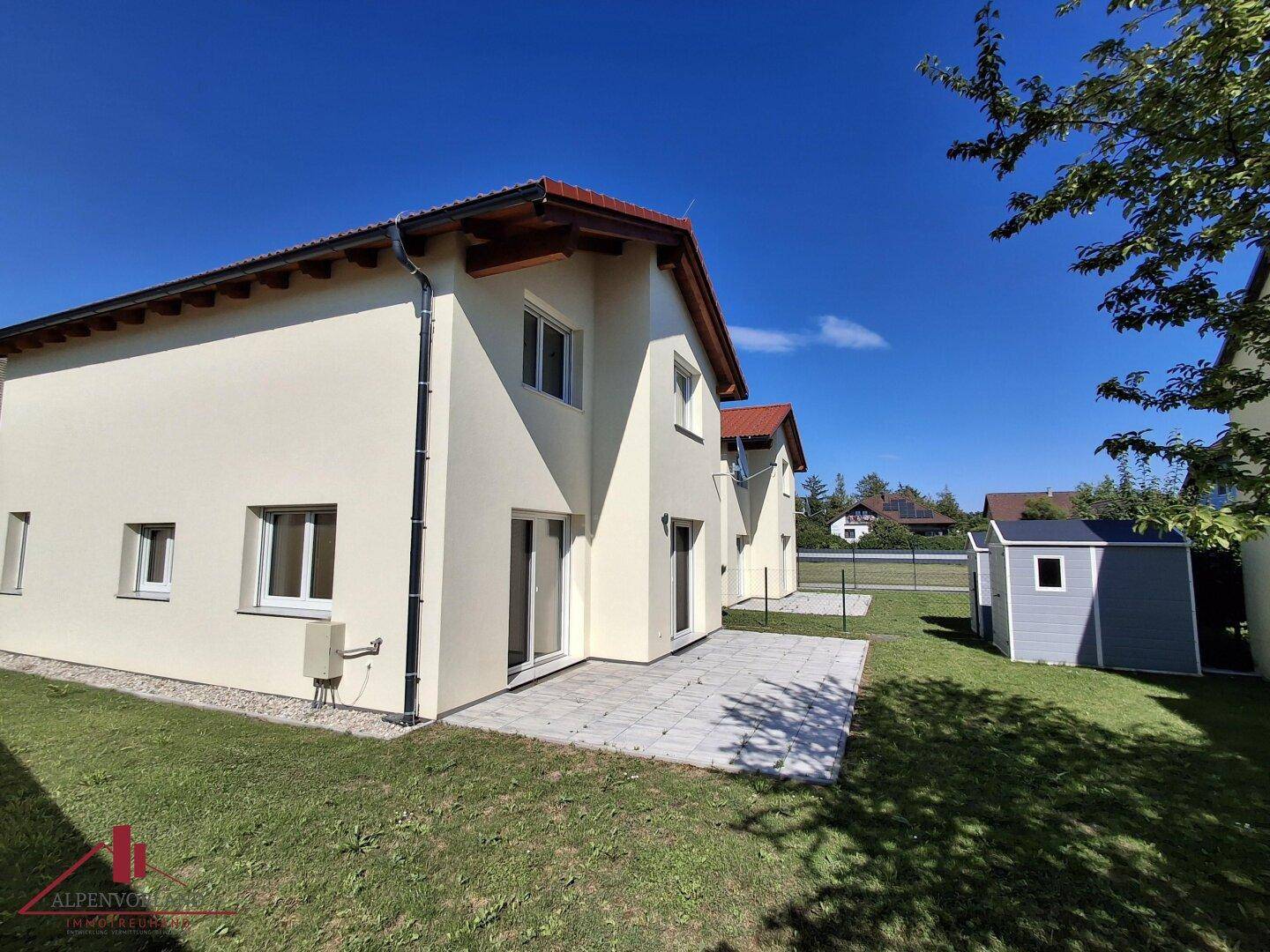 Moderne Doppelhaushälfte mit Garten, gepflasterter Terrasse und kleinem Geräteschuppen im Freien.
