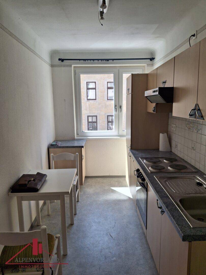 Funktionale Küche mit Einbauschränken, Herd und Spüle, inklusive kleinem Essbereich am Fenster.