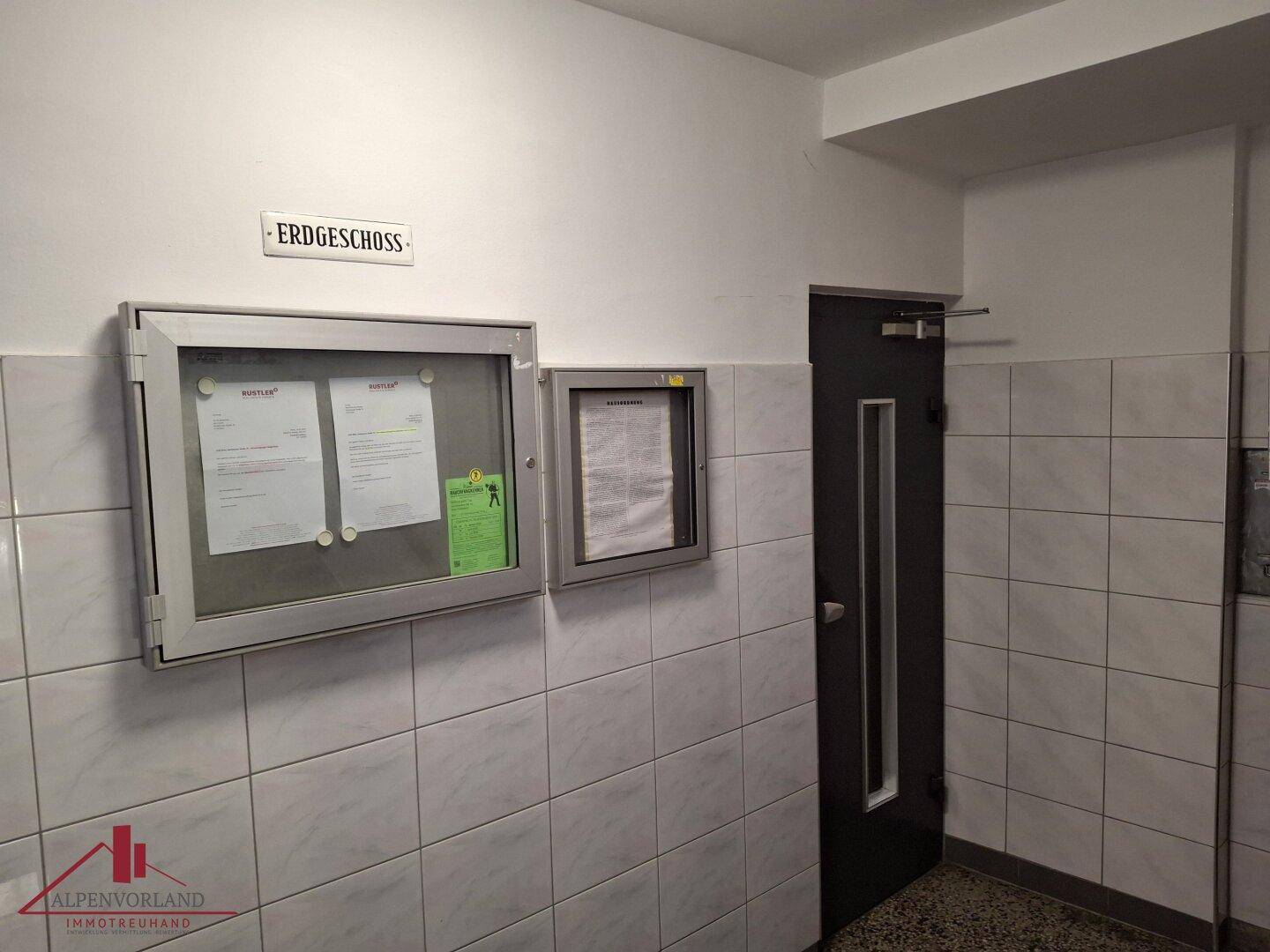 Eingangsbereich im Erdgeschoss mit Fliesenwänden und Informationsaushängen.