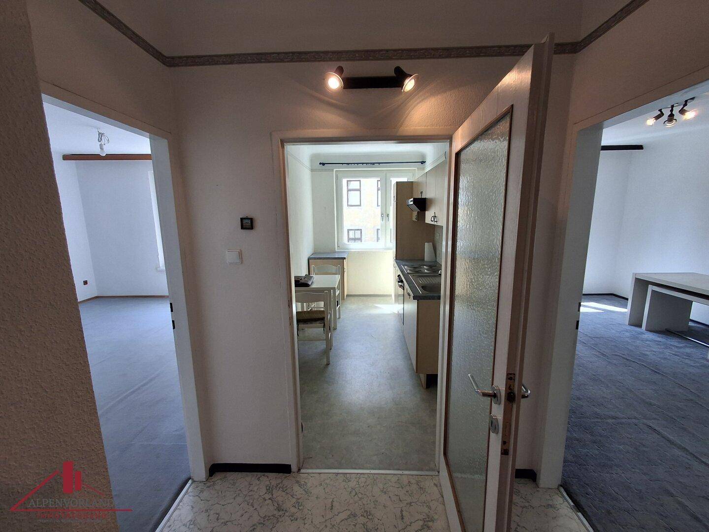 Heller Flur mit Zugang zu verschiedenen Zimmern, inklusive Blick in die Küche.