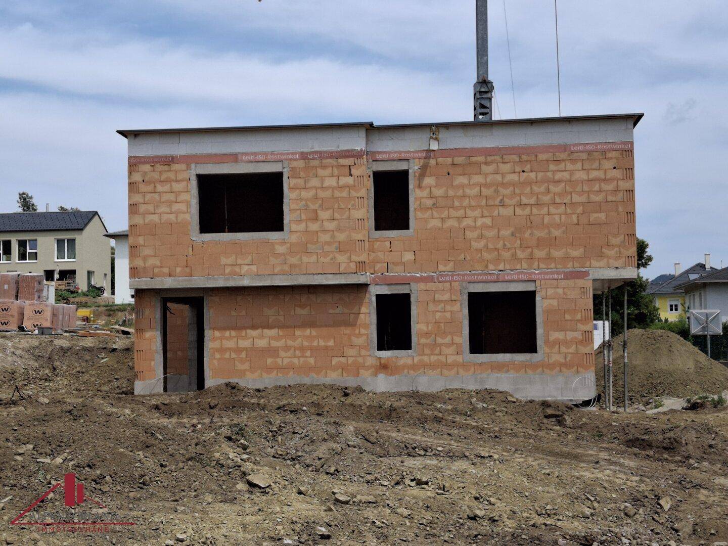 Seitenansicht eines im Bau befindlichen Hauses mit Ziegelwänden und leeren Fensteröffnungen.