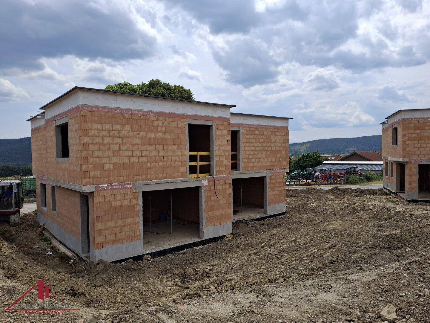 Zwei Rohbauten auf einer Baustelle, die die massive Ziegelbauweise und die zukünftigen Fenster zeigen.