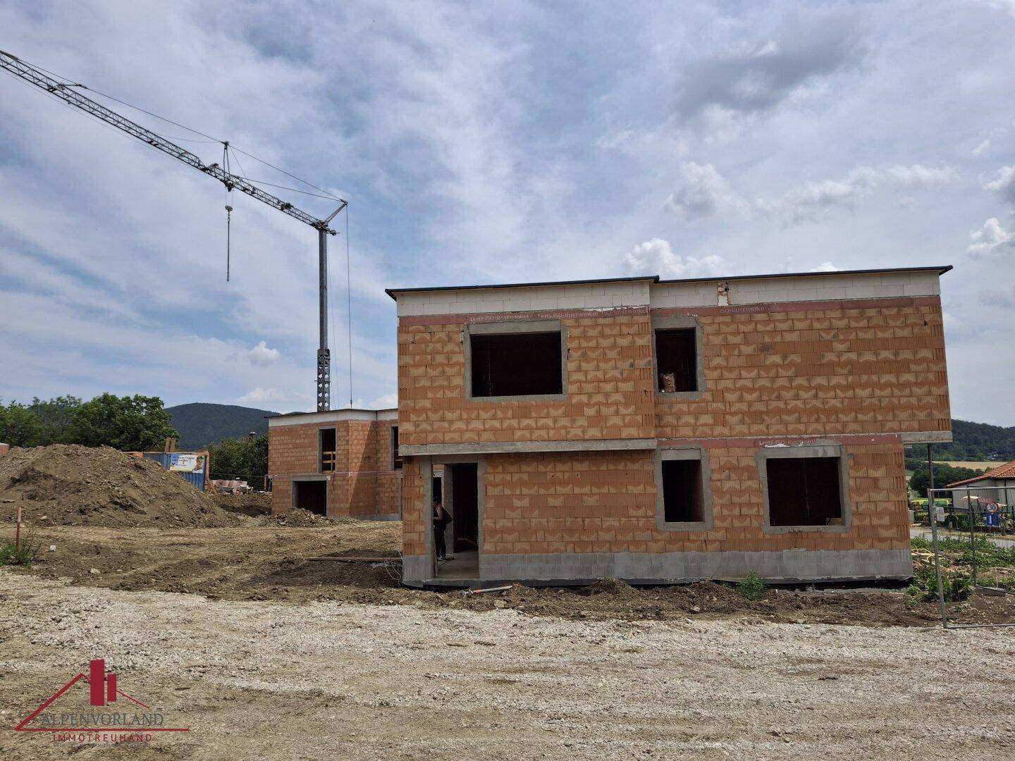 Weitläufige Baustelle mit mehreren Rohbauten und einem Baukran im Hintergrund unter blauem Himmel.
