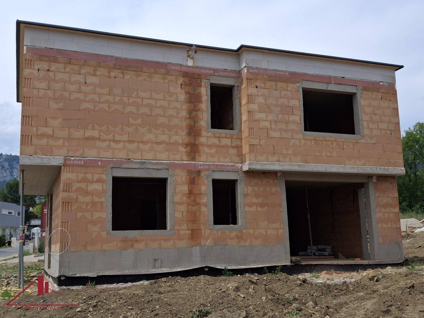 Rohbau eines modernen Einfamilienhauses mit Ziegelmauerwerk und großen Fensteröffnungen auf einer Baustelle.