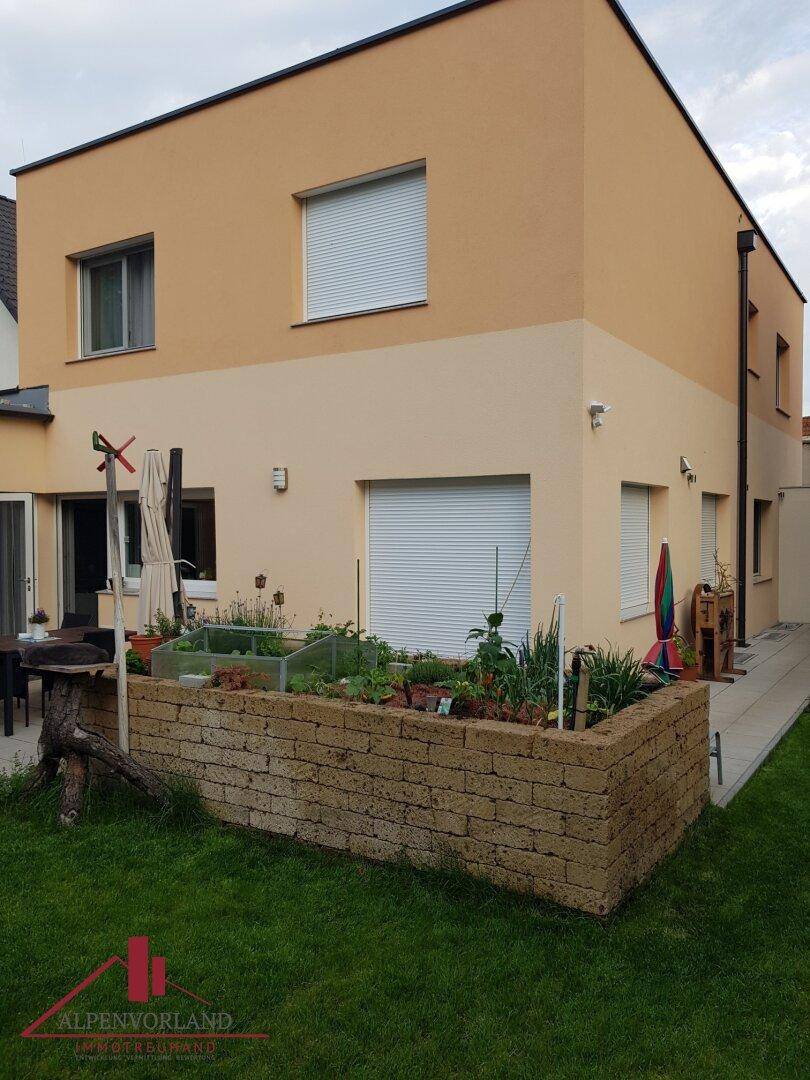 Rückseite des Hauses mit einem gepflegten Hochbeet und einer kleinen Terrasse für Mahlzeiten im Freien.