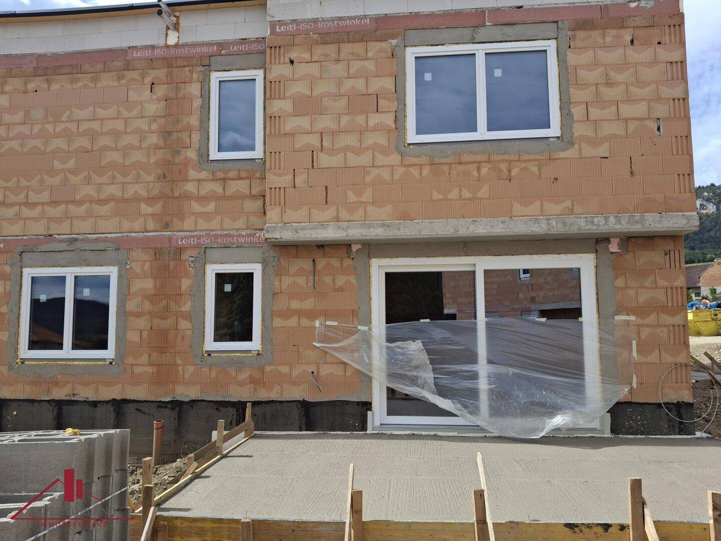 Detailansicht der Fassade im Rohbau mit installierten Fenstern und Schiebetür zur zukünftigen Terrasse.