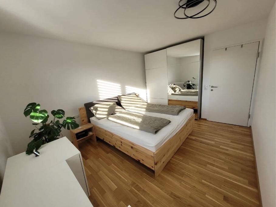 Helles Schlafzimmer mit Holzbett, großem Spiegelschrank und natürlichem Lichteinfall.