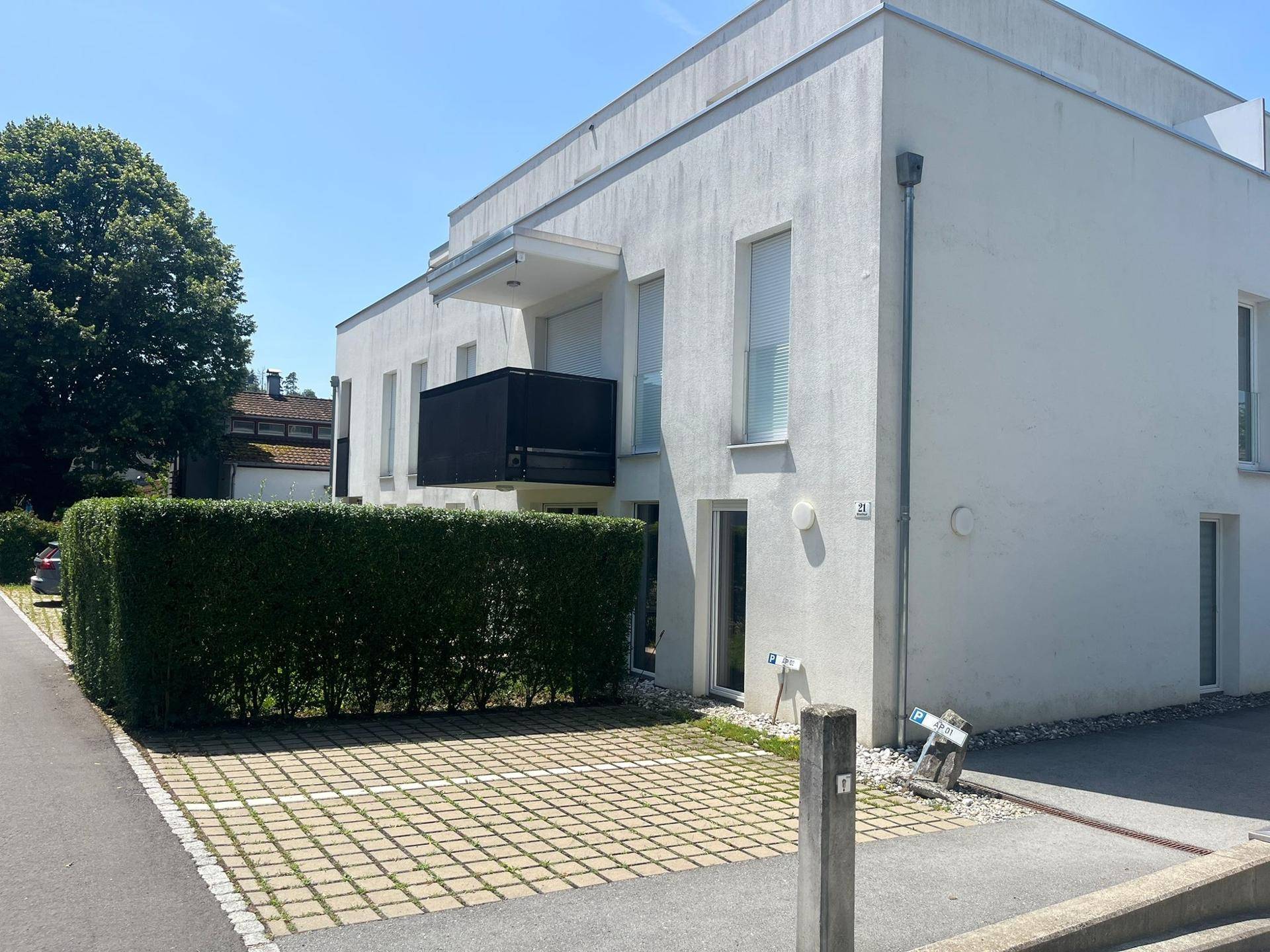 Ansicht des modernen Gebäudes von der Seite mit Parkplätzen und einer grünen Hecke vor der Fassade.