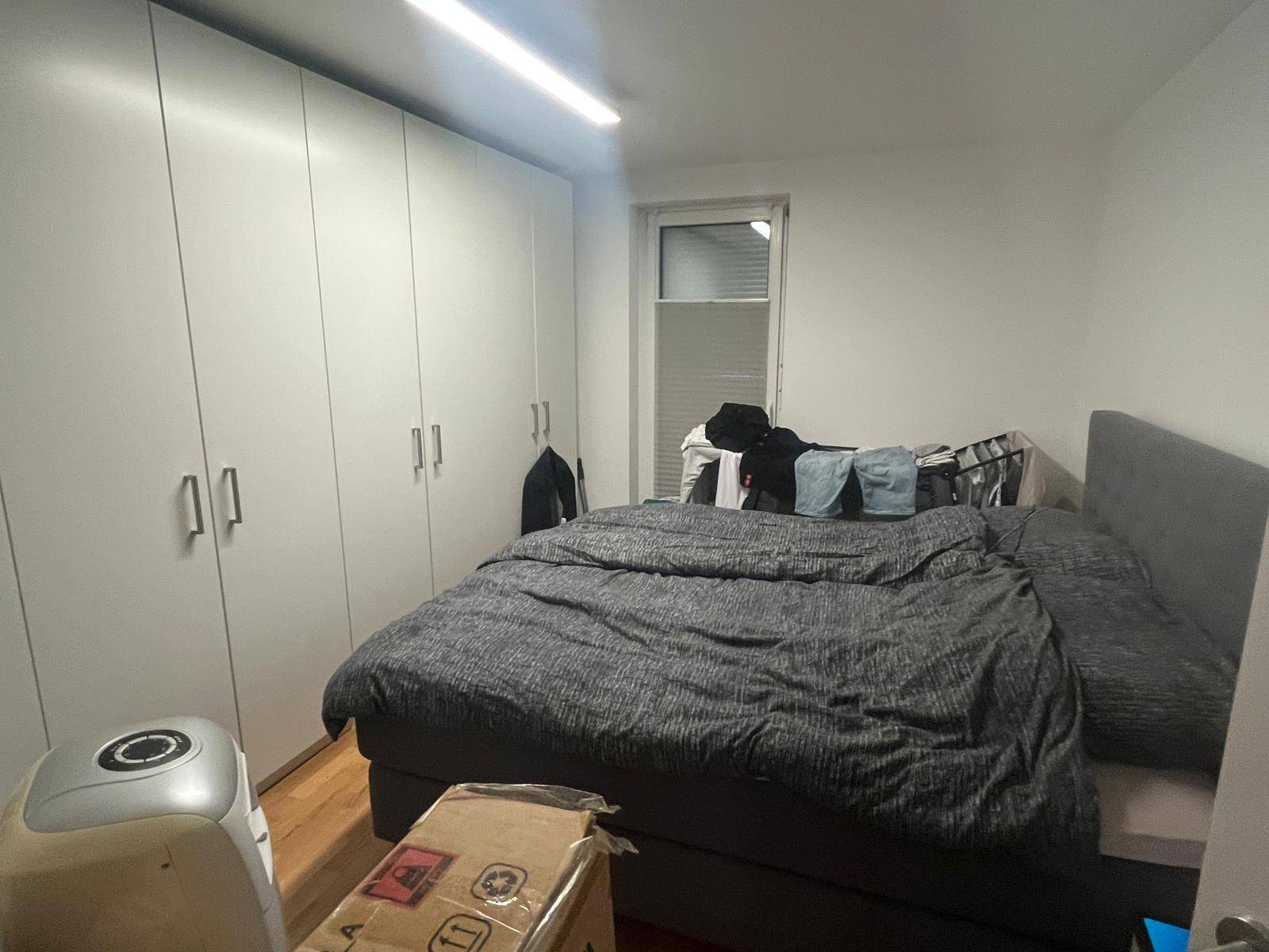 Schlafzimmer mit großem Bett, weißen Einbauschränken und einem Fenster für natürliches Licht.