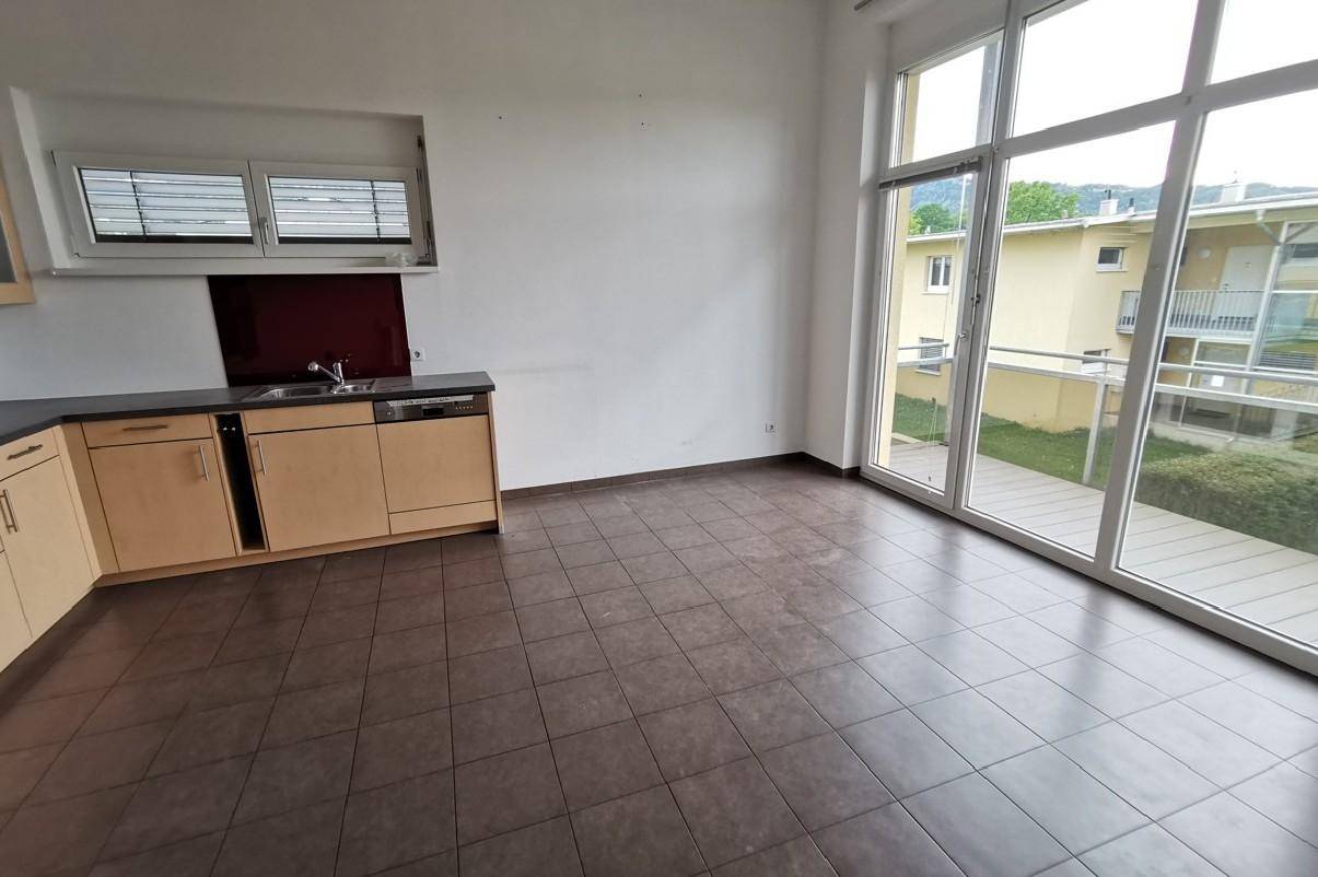 Heller Küchenbereich mit Fliesenboden und Zugang zu einem Außenbereich durch große Fenster.