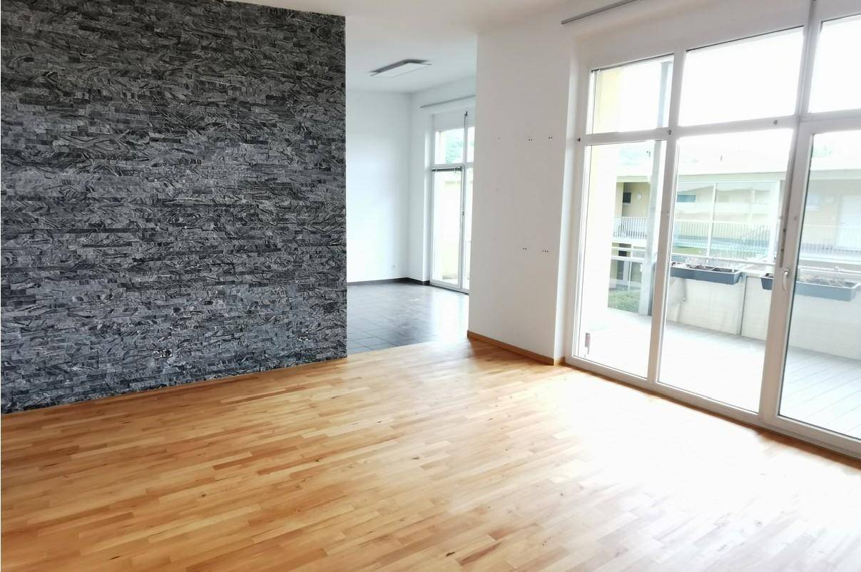 Helles Wohnzimmer mit Parkettboden und einer dekorativen Steinwand, Zugang zum Außenbereich.