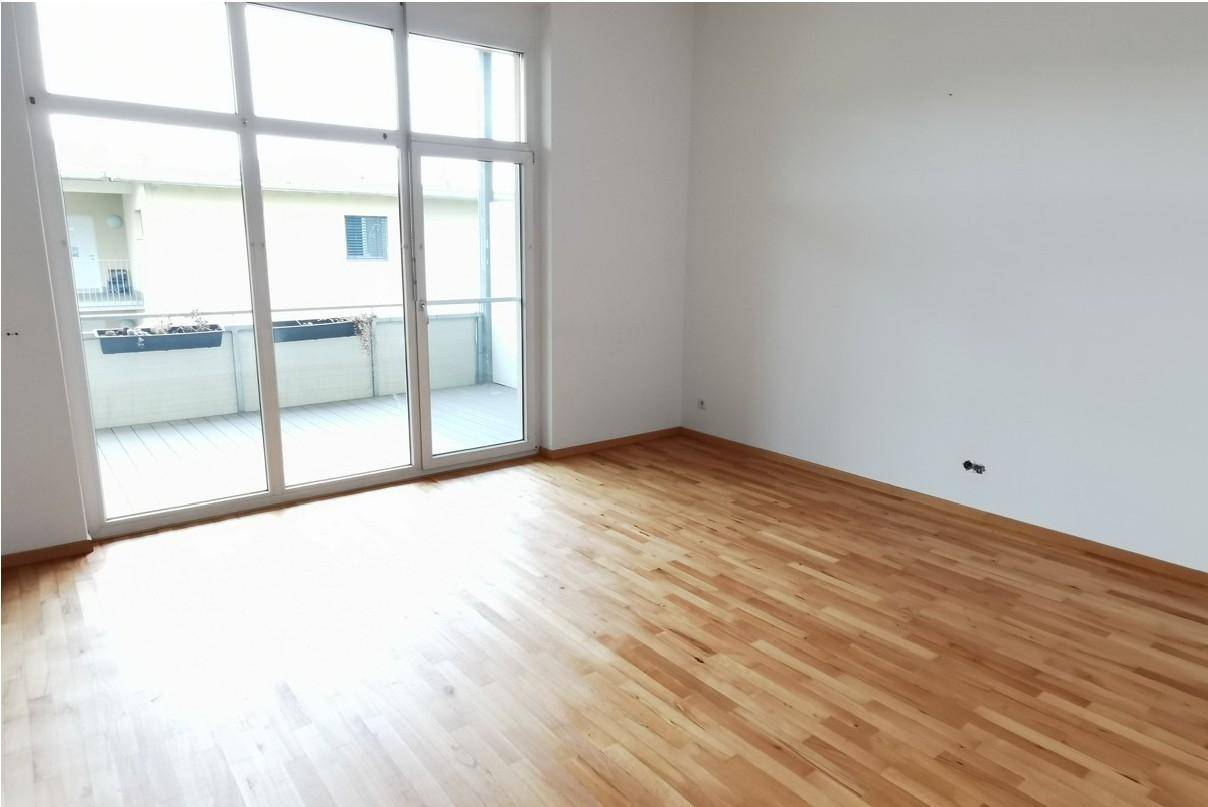 Geräumiges Wohnzimmer mit hellem Parkettboden und großen Fenstern zum Balkon.