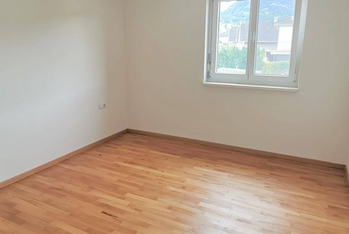 Helles Schlafzimmer mit Parkettboden und Fenster mit Blick auf die Umgebung.