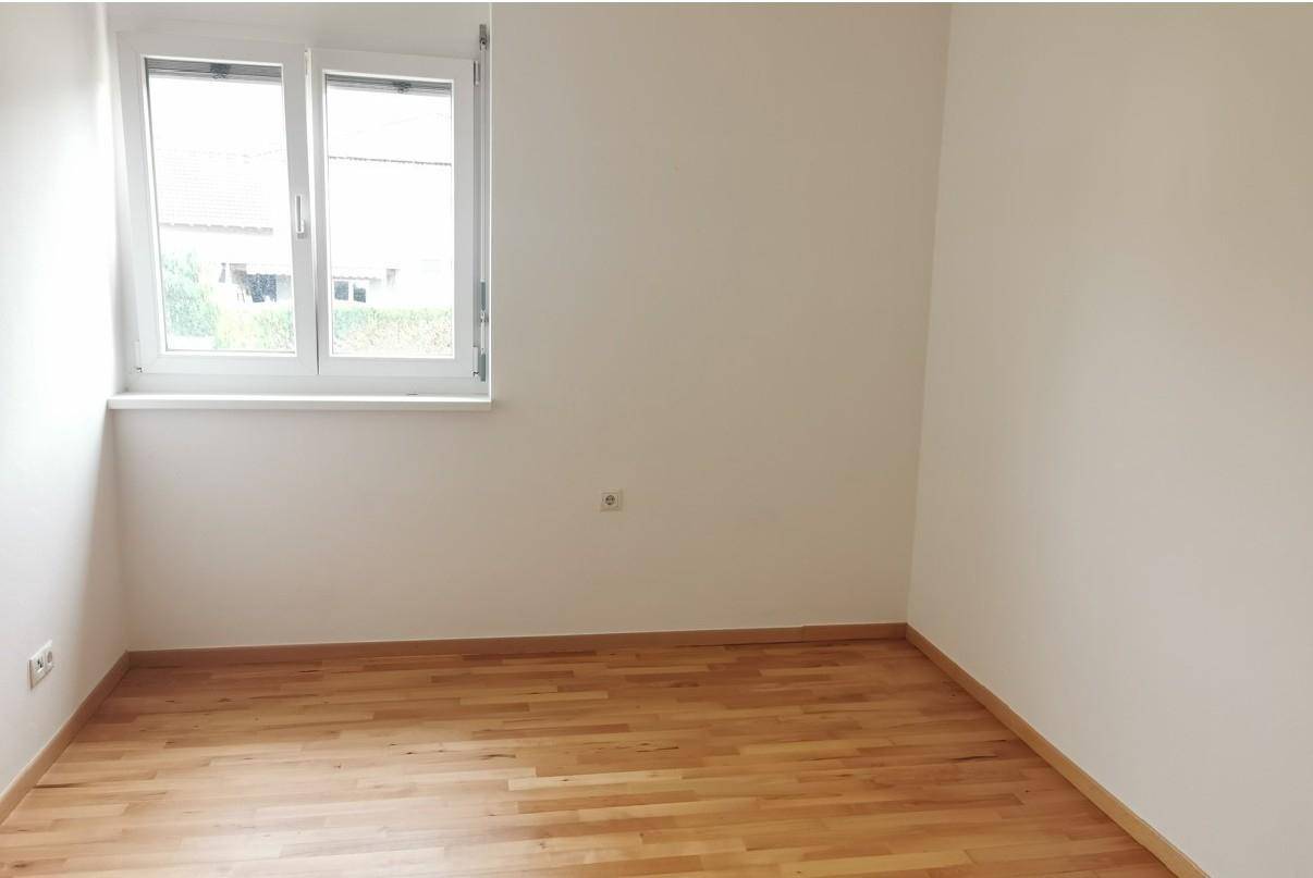 Leeres Schlafzimmer mit hellem Parkettboden und einem großen Fenster für viel Tageslicht.