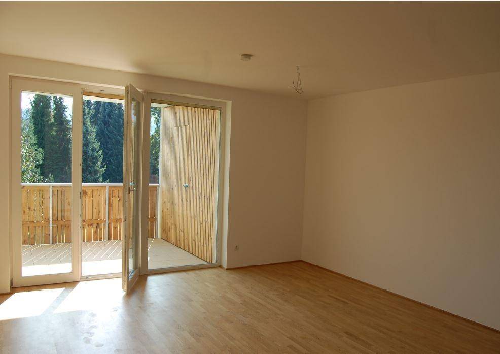 Heller Wohnraum mit Holzboden und Zugang zu einem Balkon mit Blick ins Grüne.