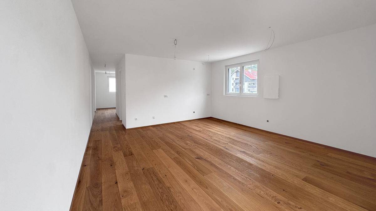 Heller, leerer Wohnraum mit neuem Holzboden und großen Fenstern, bereit zum Einzug.